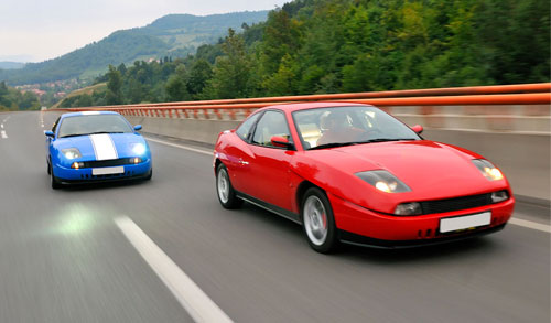 Two cars, one red, one blue driving down the highway.