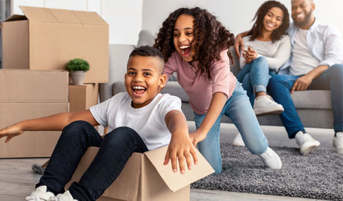 Children playing in moving boxes while adults look on.