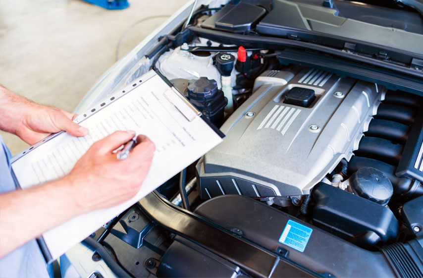 Man uses clipboard to make notes on clipboard while standing over auto engine.