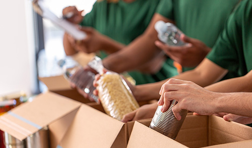 People volunteering at food bank placing items into boxes.